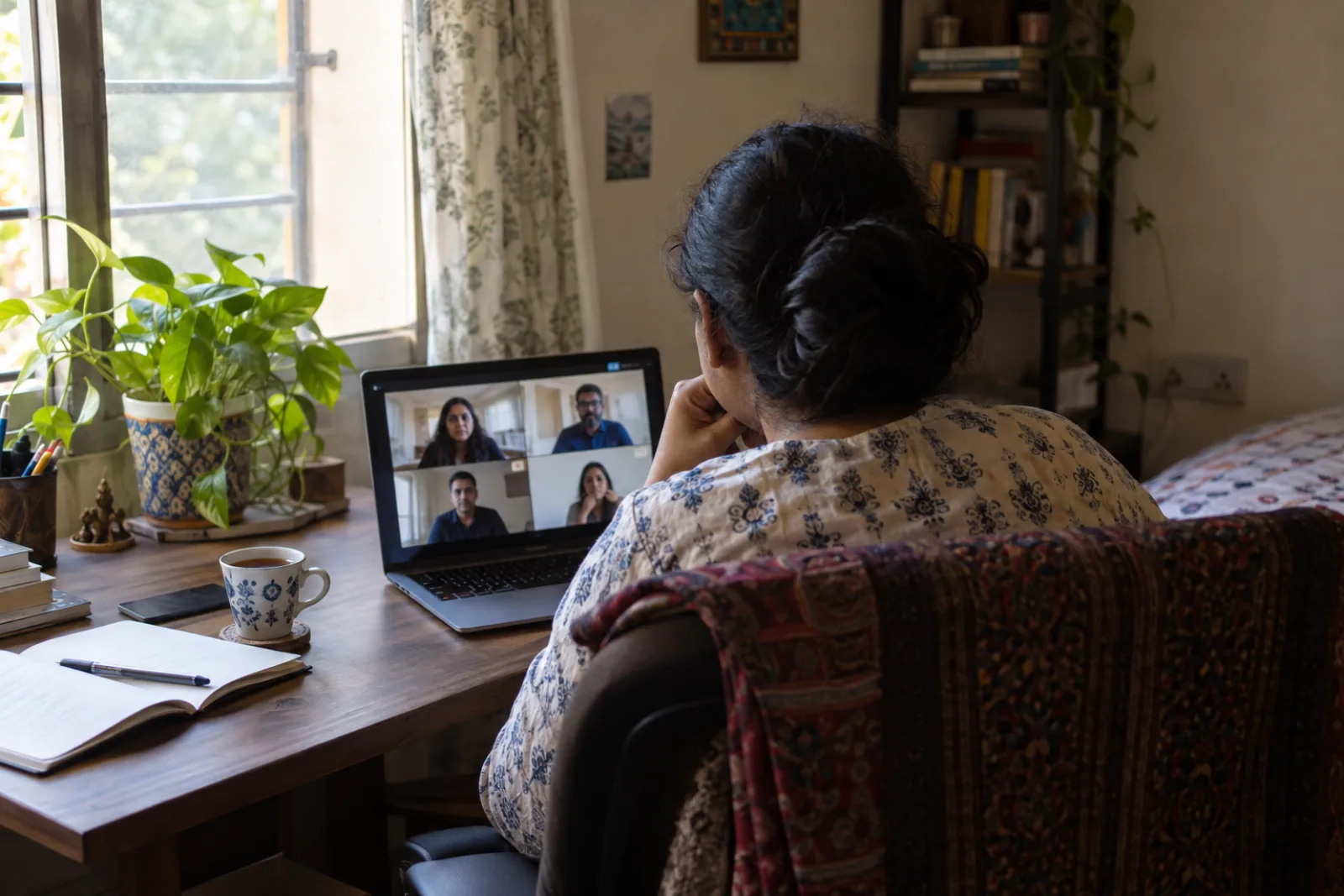 A consultant on a laptop video call in a small home office, seen from behind (illustrative photo)